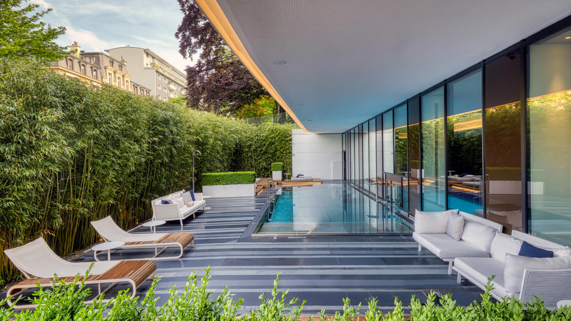 Serene outdoor pool area with sleek white furnishings and lush greenery, evoking relaxation and luxury in urban design.