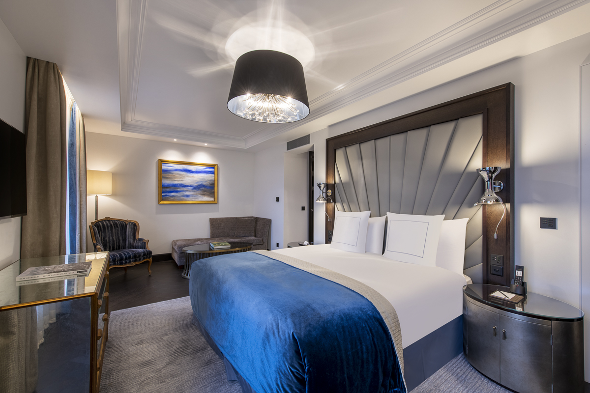 Elegant hotel room with a plush blue velvet bed, sophisticated lighting, ideal for a luxurious hospitality experience.