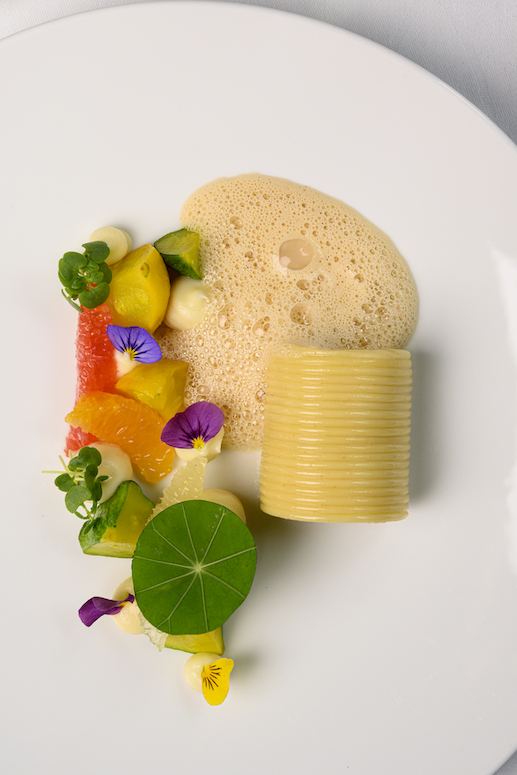 Artistic gourmet dish with vibrant fruits, edible flowers, and delicate foam, exuding freshness and creativity for culinary enthusiasts.