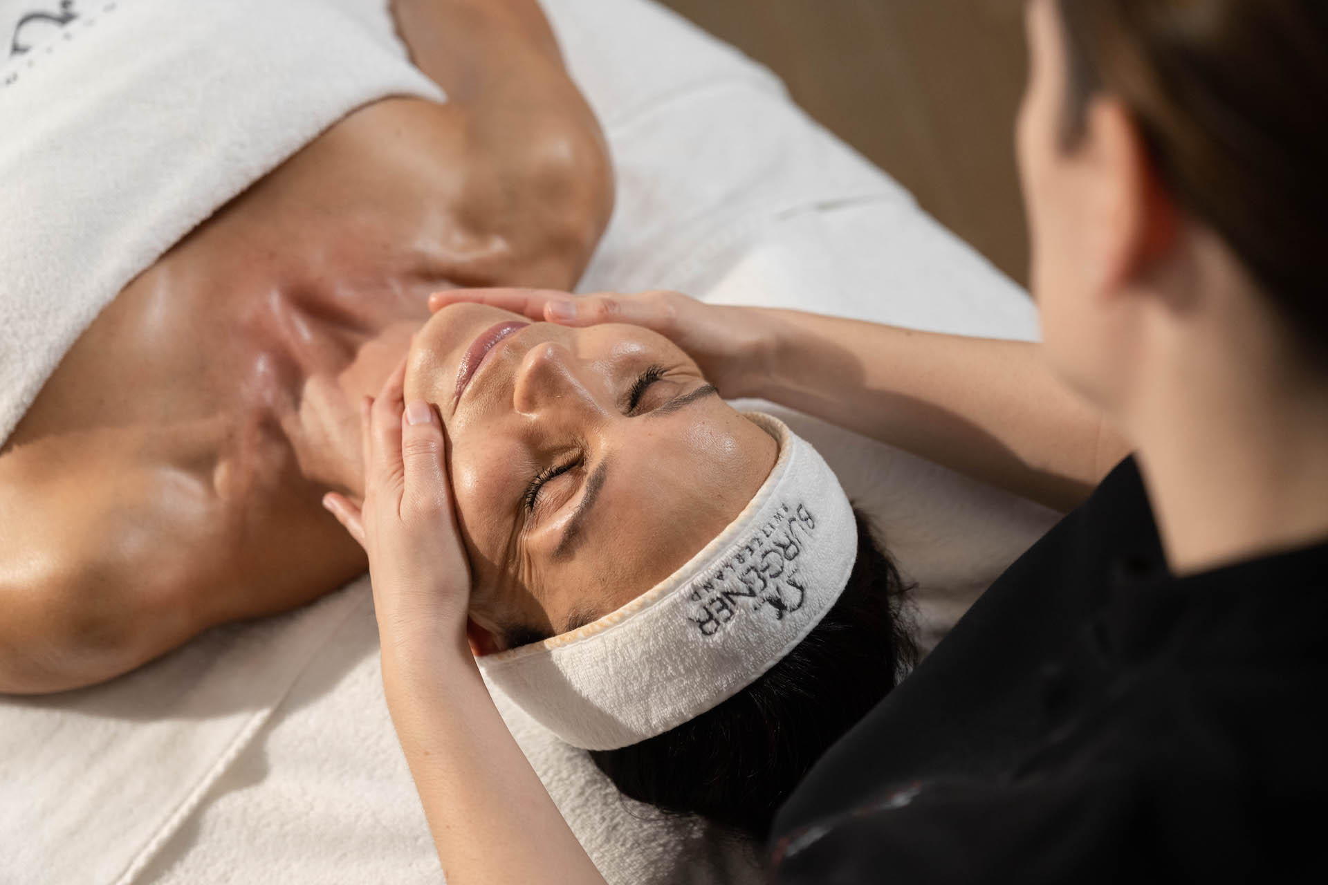 Relaxing facial treatment at a spa; a woman enjoys a soothing massage in a serene white environment, ideal for wellness industry professionals.