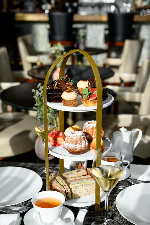 Elegant afternoon tea setup with a variety of pastries and sandwiches, set in a sunlit, upscale café--perfect for a relaxing break.