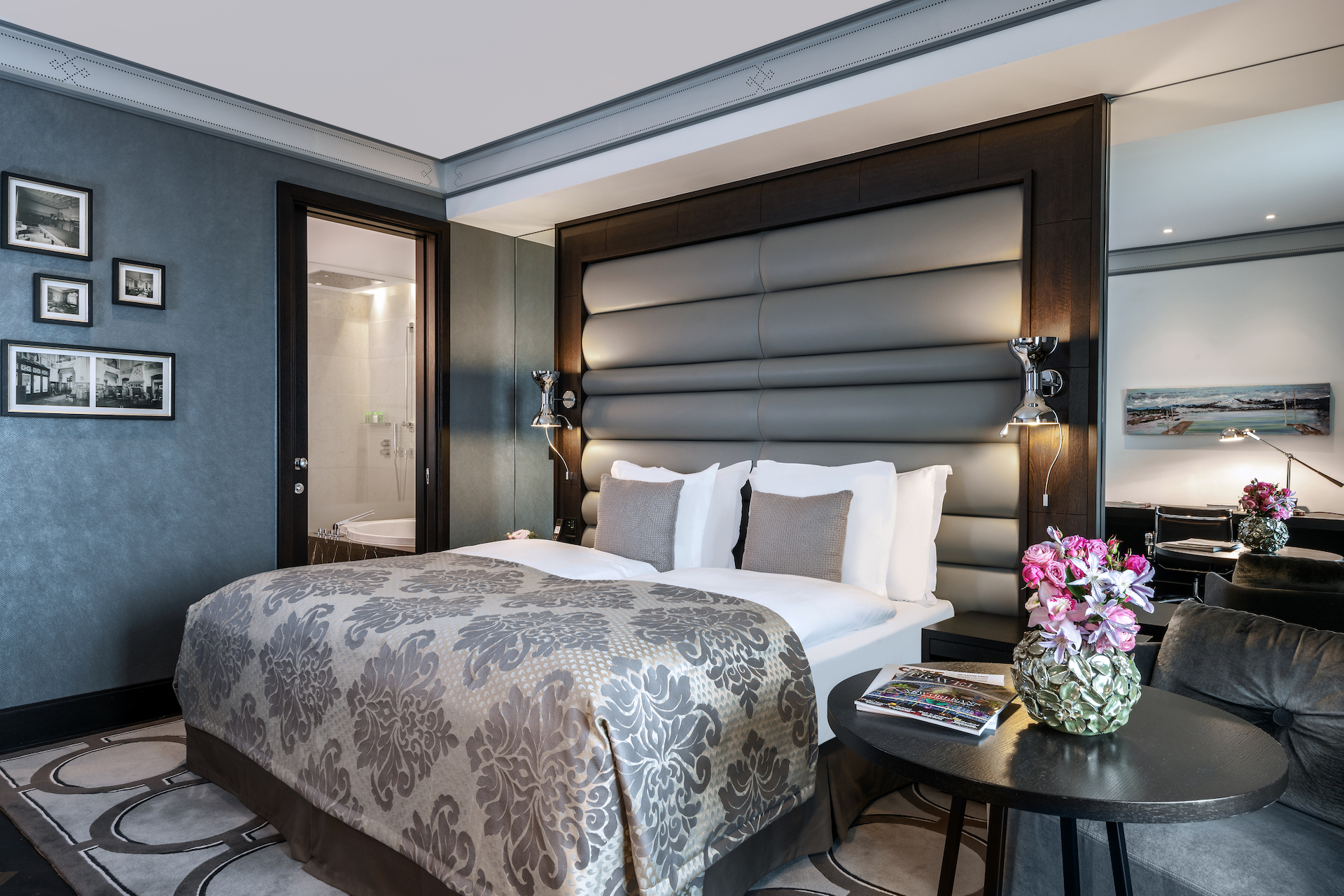 Elegant hotel room with a plush gray headboard and floral accents, showcasing a serene and luxurious ambiance ideal for travelers.