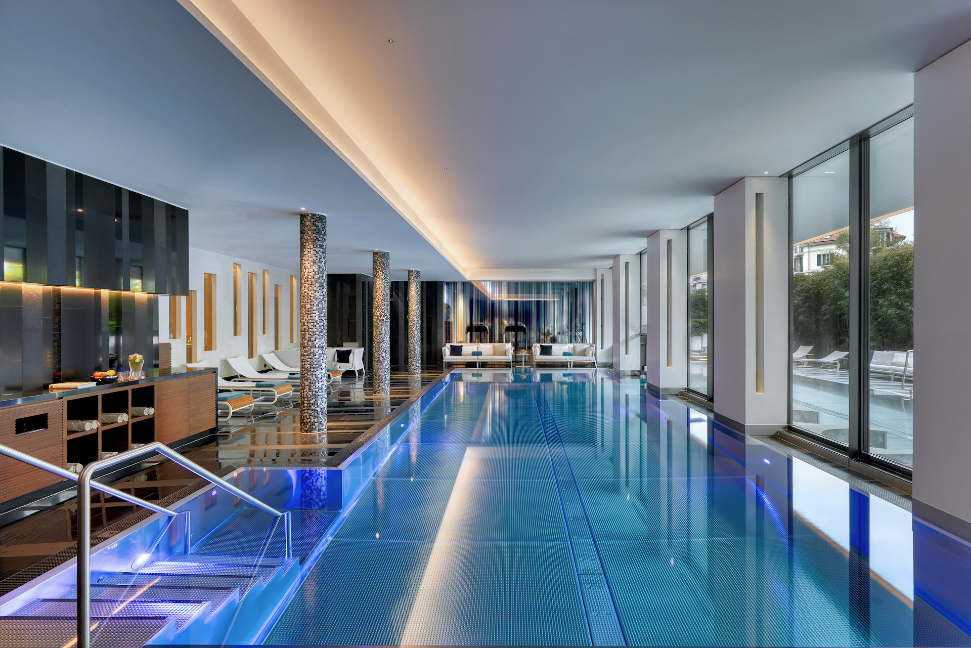 Sleek indoor pool with blue lighting and modern decor, evoking a serene and luxurious ambiance for leisure travelers.