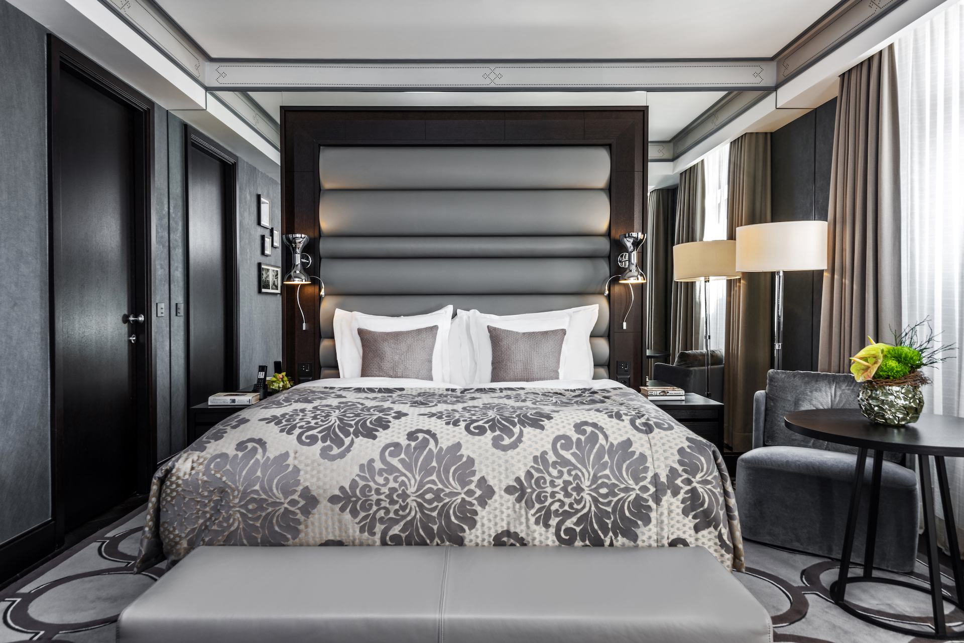 Elegant hotel room with a plush gray and cream bed, dark wood accents, and soft lighting, exuding a calm, inviting atmosphere for travelers.