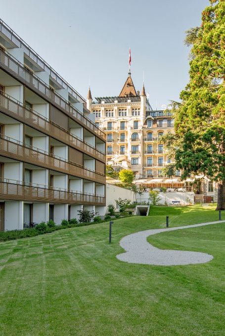 Path-lined green lawn meeting modern apartments, with a historic tower building in the background, evoking a serene blend of old and new in urban living.