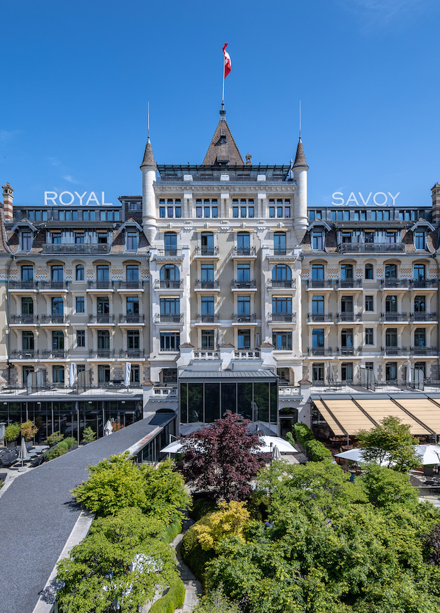 Elegant Royal Savoy Hotel facade with creamy white architecture and dark rooftops, exuding grandeur and sophistication in hospitality.