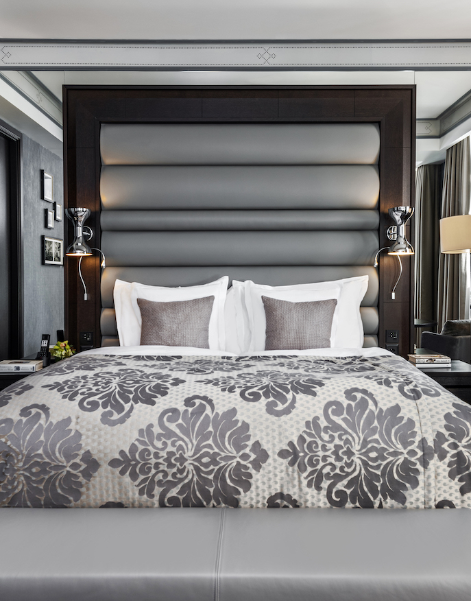 Elegant and serene hotel room featuring a patterned grey comforter and dark wooden headboard, ideal for a relaxing retreat.