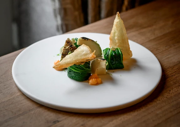 Artfully presented gourmet dish with vibrant greens and crisp garnishes on a pristine white plate, expressing elegance and culinary creativity.