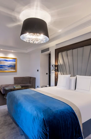 Plush hotel room with a striking blue velvet bedspread and elegant overhead lighting, offering a serene and sophisticated retreat for travelers.
