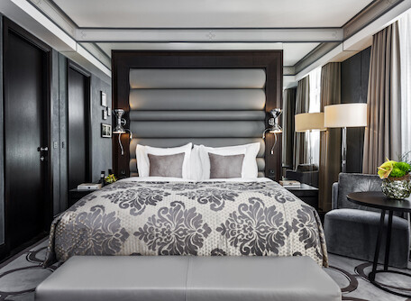 Elegant hotel room with a plush patterned bedspread and sleek, dark wood furnishings, creating a serene and sophisticated ambiance for travelers.