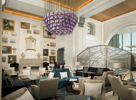 Elegant hotel lobby with plush blue and beige seating, ornate chandeliers, and curated art, exuding sophistication for the hospitality sector.