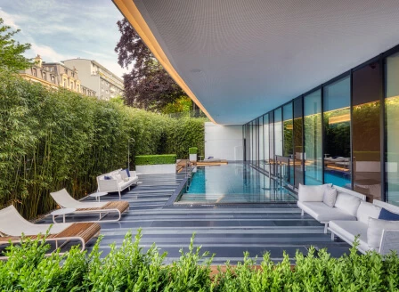 Sleek outdoor pool area with glass walls and lush greenery, exuding tranquility and modern design for luxury living.