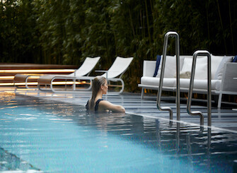 Woman relaxing in a tranquil, blue-lit pool at dusk; evokes serenity and luxury, appealing to wellness and travel sectors.