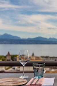 Outdoor dining setup with a clear wine glass and blue tumbler, overlooking a serene lake scene, evoking relaxation and elegance in hospitality.