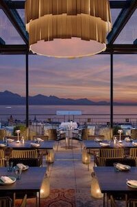 Elegant restaurant with golden lighting and wooden furnishing, radiating warmth and sophistication against a mountainous sunset view.