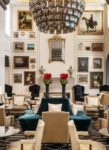Opulent hotel lobby adorned with a dramatic chandelier, richly framed artwork, and plush seating, evokes a luxurious and welcoming ambiance for travelers.